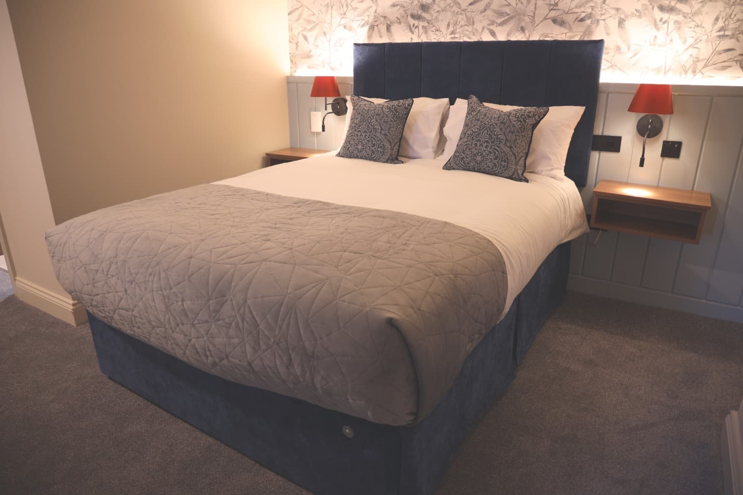 King bed with deep blue velvet headboard and brass-toned sconces