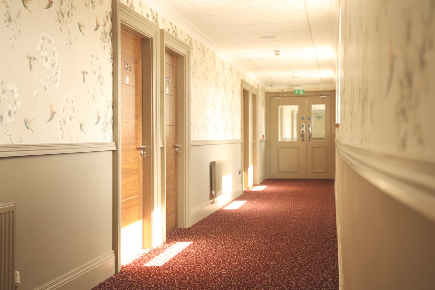 Wallpapered corridor with timber doors and a deep ruby carpet